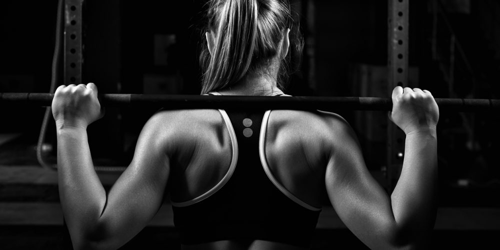 Squat - image of the back view young female doing barbell squats in gym