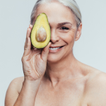 Longevity through Nutrition - woman holding a halved avocado over one eye