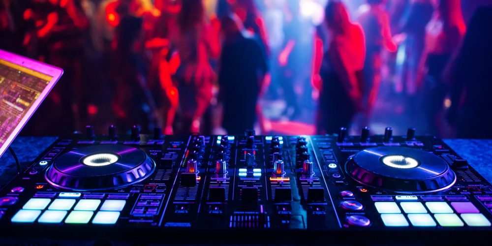 making music for fitness classes - Image of controller DJ mixer in a nightclub at a party against the background of blurred silhouettes of dancing people