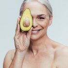 Longevity through nutrition - image of smiling woman holding up an avocado in front of one of her eyes
