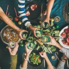 Flat-lay of human hands holding glasses with drinks, feasting and celebrating holiday together, top view - food combining part one